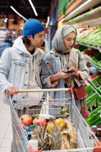 Casal escolhendo produtos no supermercado com carrinho de compras cheio, representando planejamento de orçamento familiar