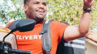 Entregador sorridente em motocicleta fazendo gesto com a mão, representando trabalho por aplicativo como renda extra