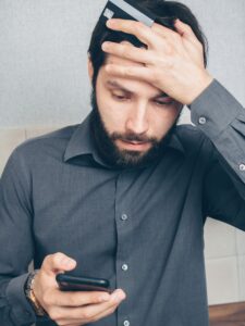 Homem preocupado olhando para o smartphone enquanto segura o cartão de crédito, representando alerta de golpe