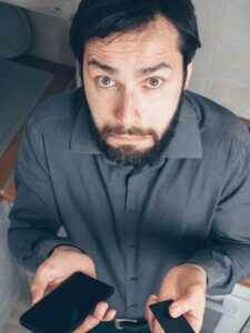 Homem confuso segurando cartão de crédito e olhando para o celular, representando dúvida sobre dívida no rotativo